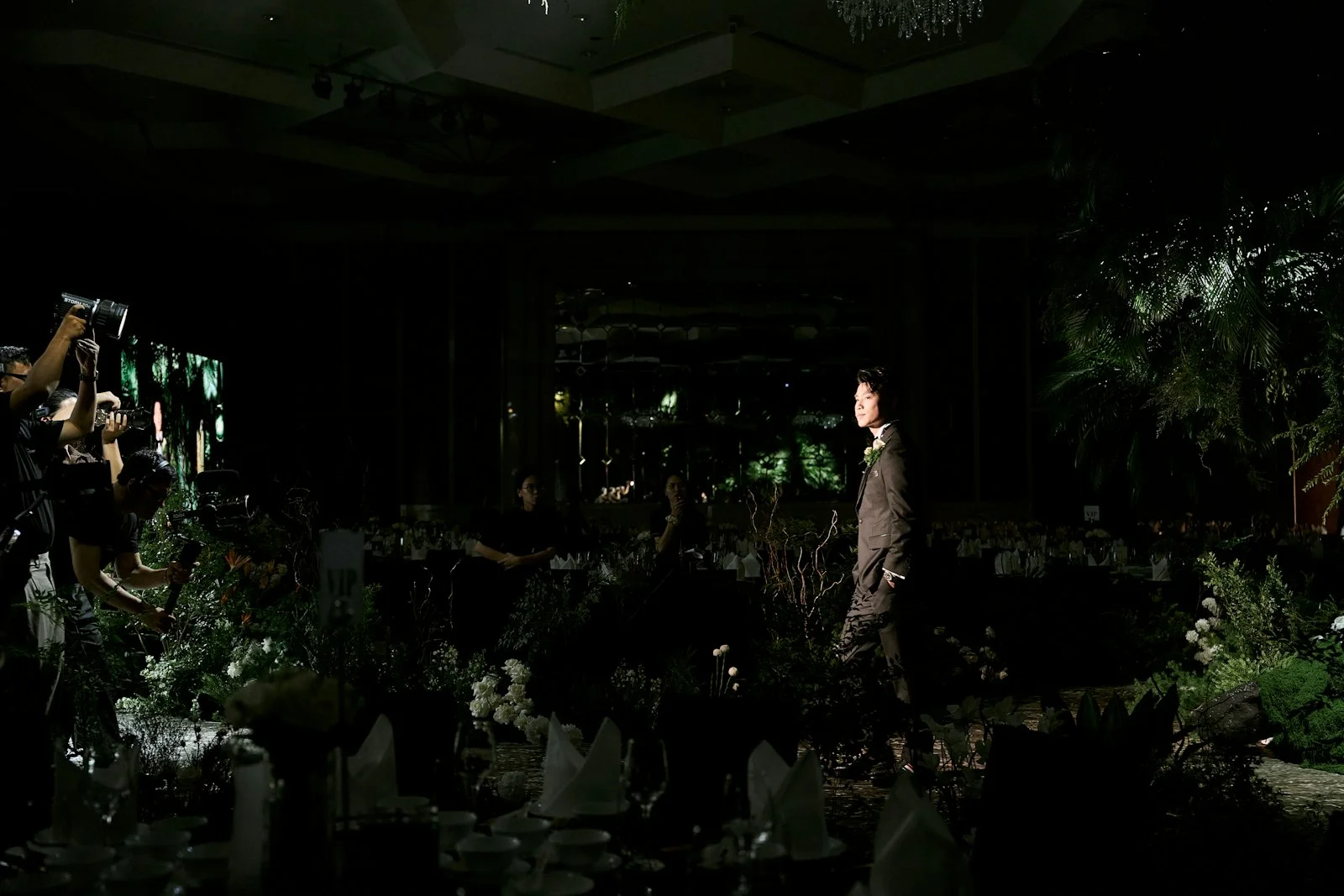 Figure walks on a dark runway amidst lush green foliage